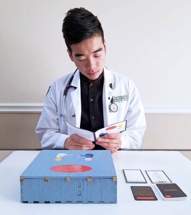Person with labcoat and stethoscope reading a pamphlet at a table with a box on it